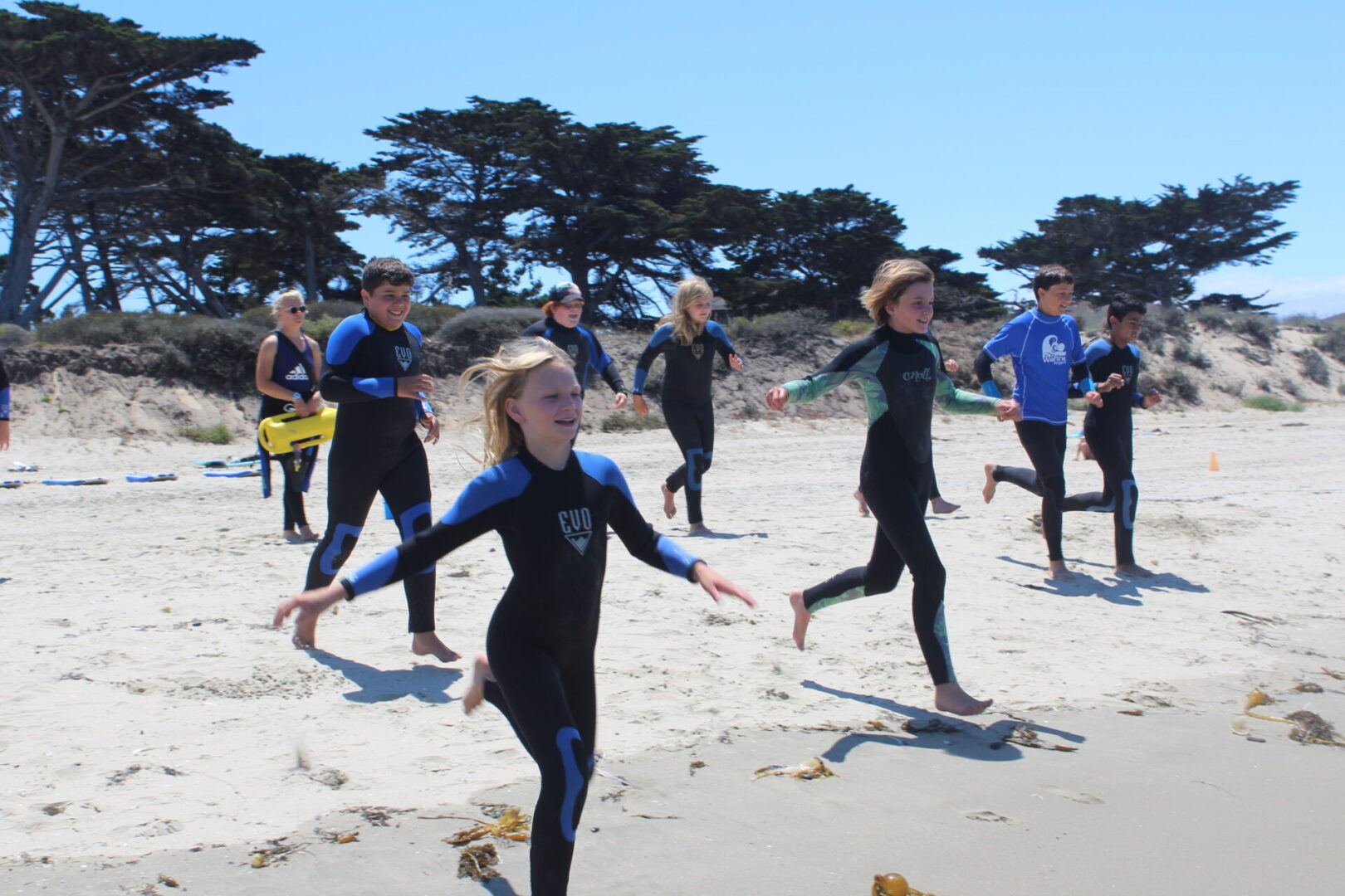 A group of people in wetsuits running on the beach.