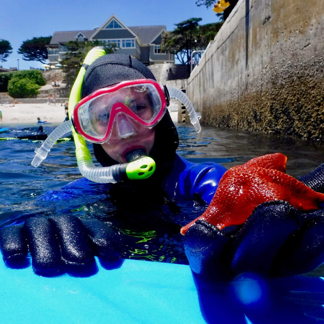 A person in a wet suit and goggles on a surfboard.