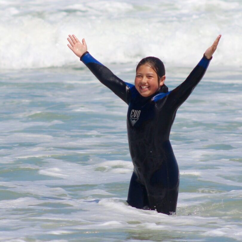 A girl in the ocean waves with her arms up.