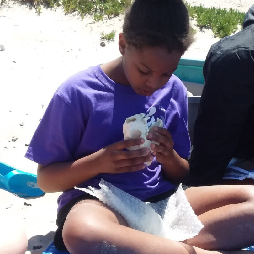 A boy sitting on the beach eating food.