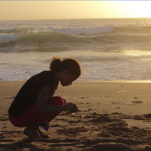 A woman kneeling down on the beach looking at waves.