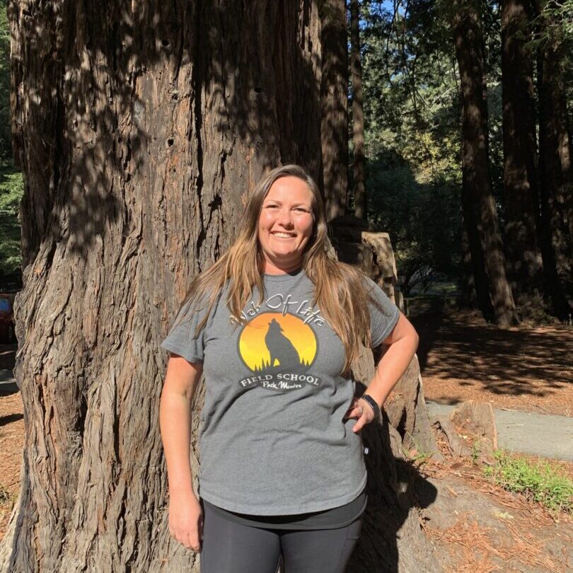 A woman standing next to a tree in front of some trees